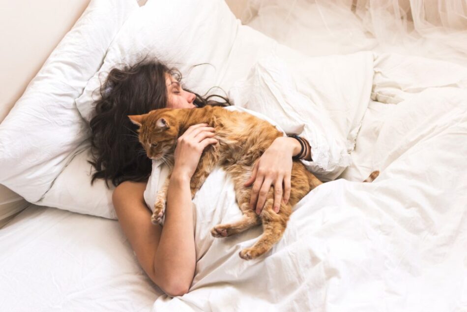 En kvinna sover på en säng tillsammans med sin katt