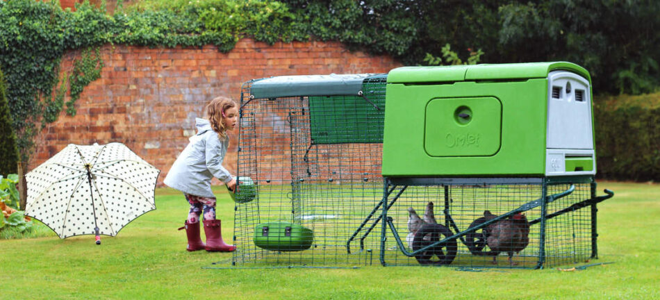 En flicka matar sina hönor som är i ett grönt Eglu Cube-hönshus med hönsgård