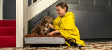 En flicka klappar en brun hund som ligger på hundsängen Topology med en bäddmadrass i mikrofiber